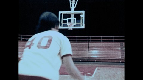 1970s: Shots of girls playing basketball in gym. Girl dribbling ball, makes shot, zoom in on basket. Slow motion, girl pivoting feet.