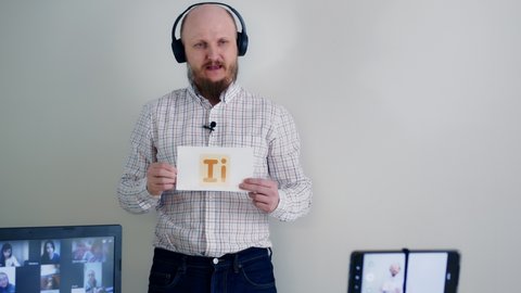 Learning English remotely online. A bald man with a beard wearing headphones and a microphone conducts a grammar lesson using flashcards to learn letters. remote learning
