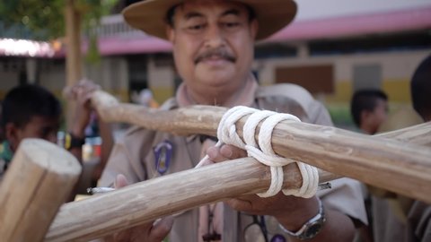 Yala, Thailand March 11, 2016  Thai Boy Scout activities teacher in uniform making wooden catapult teach students to build a frame, attach sticks with a rope Ban Yala primary school