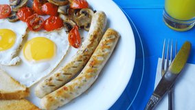 4k loop video of a breakfast of fried eggs, mushrooms, tomatoes, sausages and bread, rotating on a white plate on a wooden blue table.