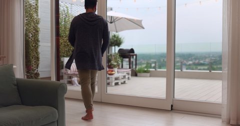 man opens sliding doors, going out on rooftop patio with cozy lounge zone and beautiful landscape view