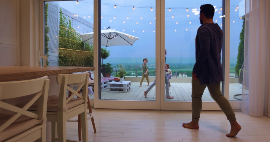 Happy man opens sliding doors, going out on rooftop patio with playing kids and beautiful landscape view | Shutterstock HD Video #1075964834