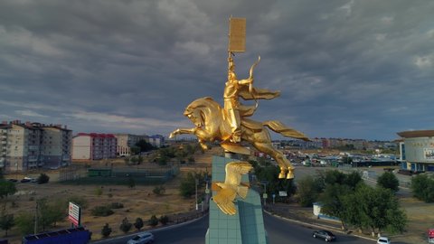 Elista, Kalmykia, Russia- 25 june 2020: Aerial golden horseman capital tourist attraction. Traditional Soviet stella in center of road junction, traffic cars ride. Epic cityscape. Dramatic clouds