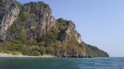 Panning dolly shot of limestone karst island, blue sky, white sand beach in Thailand. Mosquito island Koh Yung. POV of Boat moving through turquoise green ocean water of the Andaman sea near Phuket.