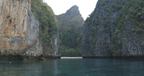 Static shot of the famous Loh Samah bay in Phi Phi island Thailand. Early morning tropical island with calm blue clear water, limestone karsts, small white sand beach, green palm trees.