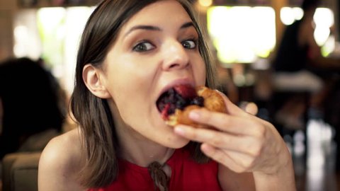 Hungry, funny woman eating tasty bun in cafe
