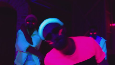 Group of female and male stylish dancers dancing inside dark place with neon lights .  Beautiful young people with fluorescent colorful make-up and clothes dancing in UV light. HD video in slow motion