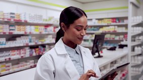 Mixed race female pharmacist typing on digital tablet smiling in pharmacy