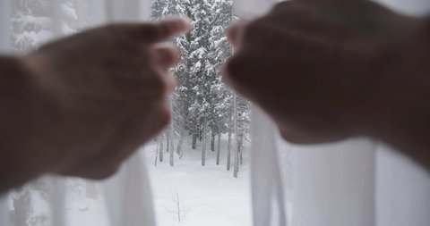 Opening window curtains to reveal snow outside and snow covered trees in a forest. Winter season, mountain home, travelling, accommodation.