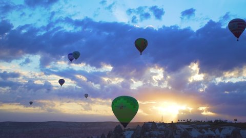 Goreme, Cappadocia, Turkey - May 28, 2021: Ballooning in Kapadokya. Many hot air balloons flying over spectacular breathtaking unusual valleys, rocks and Goreme town in blue sunrise morning sky