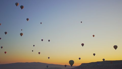 Goreme, Cappadocia, Turkey - May 30, 2021: Ballooning in Kapadokya. Many hot air balloons flying over spectacular breathtaking unusual city streets, valleys and rocks in blue sunrise morning sky