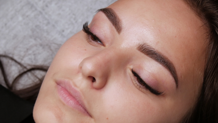 A beautiful young girl model with ready made permanent makeup for eyebrows lies on a couch at the master. Microblading, permanent makeup tattoo close up view | Shutterstock HD Video #1075978619