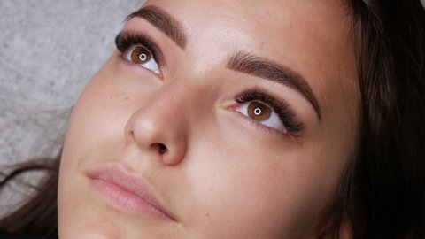 A beautiful young girl model with ready made permanent makeup for eyebrows lies on a couch at the master. Microblading, permanent makeup tattoo close up view