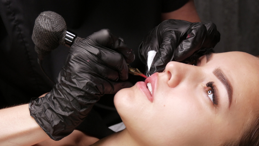 Microblading lip tattoo with special coloring red pigment that corrects lip color in cosmetology clinic. Permanent makeup lips procedure applying pigment makeup on lips with a tattoo machine | Shutterstock HD Video #1075978625
