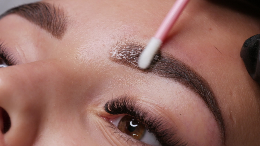 Applying a special fixing gel with a cotton swab. A beautiful young girl model with ready made permanent makeup for eyebrows. Microblading, permanent makeup tattoo close up view | Shutterstock HD Video #1075978646
