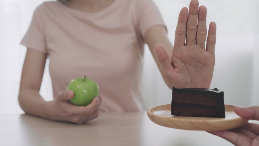 Women refuse to eat cake chocolate and choose to eat green apple. Diet for Healthy women and strong bodies. Cake have many of fat . diet concept.