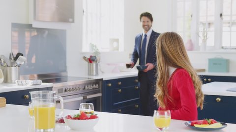 Father Wearing Suit Having Breakfast With Teenage Daughter In School Uniform At Home In Kitchen