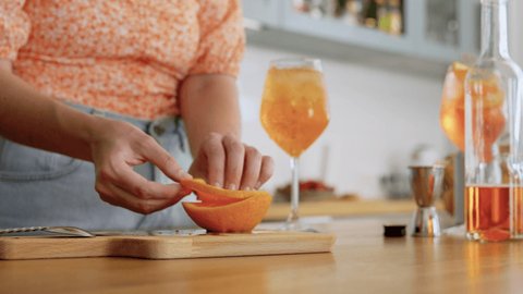 drinks and people concept - happy smiling young woman making orange cocktail at home kitchen