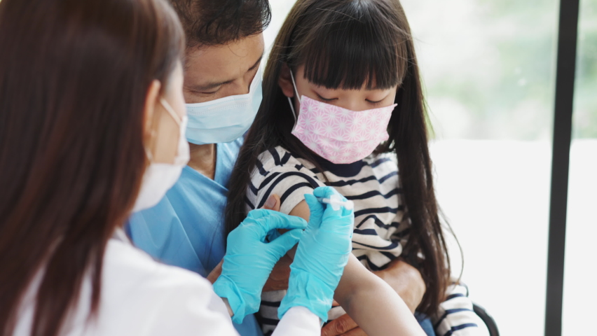 Asian  senior doctor wearing gloves and isolation mask is making a COVID-19 vaccination in the shoulder of child patient with her mother at hospital.closed up photo. Royalty-Free Stock Footage #1075988231