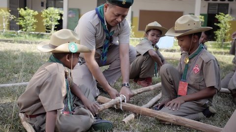 Yala, Thailand March 11, 2016  Thai Boy Scout activities students boys in uniform making wooden catapult learn to build frame, teacher teach how to attach sticks with a rope, Ban Yala primary school