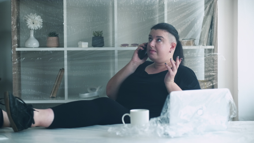 Home office. Distance work. House relocation self-isolation. Pandemic furlough. Worried woman looking for new apartment making phone call in light room covered with plastic wrap.