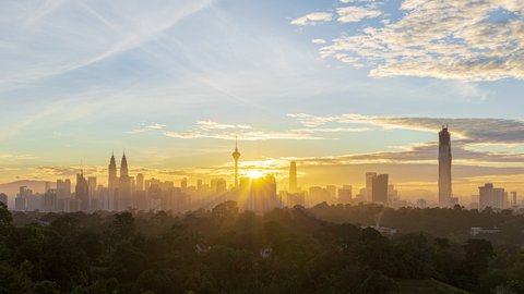 Time lapse: Silhouette of Kuala Lumpur city view during dawn overlooking the city skyline from afar with lushes green in the foreground. Federal Territory, Malaysia. Pan up motion timelapse.