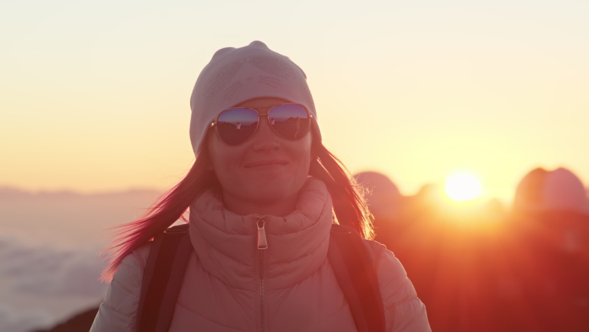 Sunshine young smiling woman with pink hair looking at camera. Slow motion portrait happy girl face at golden sunset on top of mountain above clouds. Close up beautiful smile lady outdoors 4K winter