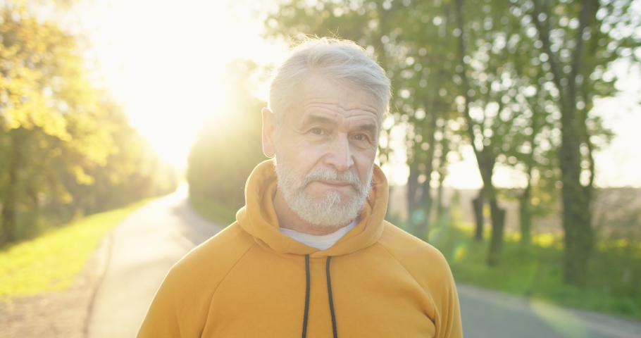 Close up portrait of joyful positive Caucasian handsome old man in good mood smiling at camera standing on street in sun lights in the morning. Happy senior male with smile on face, outdoor concept Royalty-Free Stock Footage #1075999283