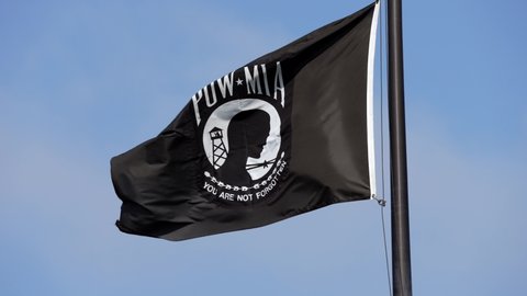 This slow motion video shows a POW MIA flag flying in the wind against a clear blue sky.