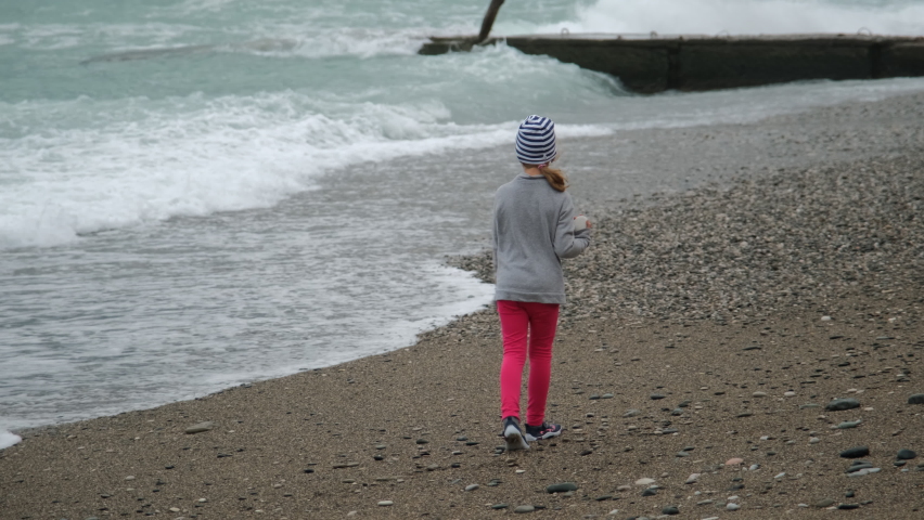 Little Girl Walking Along the Rough Seashore. Back View. Travel, Tourism, Vacation at Sea and People Concept