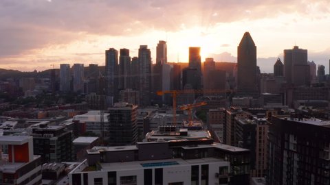 Aerial Drone of Downtown Montreal Sunset with Sun Rays Shining Through Tall Buildings. Construction and Cranes Seen in Distance. 