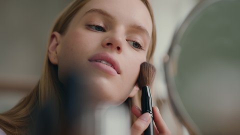 Young woman applying everyday makeup and preparing go out. Nude make-up of stylish girl or daily care for clear face of cute 20s lady. Morning visage of casual model looking at mirror at home closeup