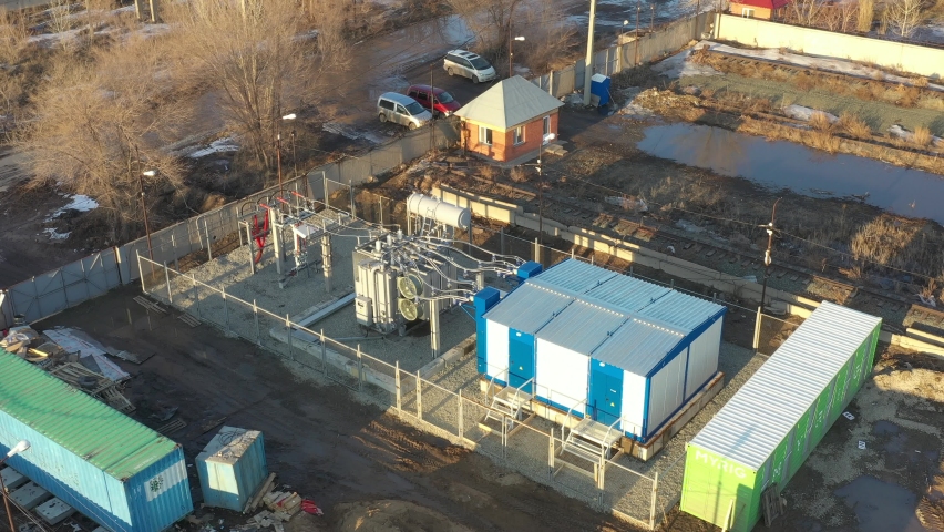 Aerial over power transformer with cables at electrical distributing substation on sunny day. Active cooling fan on modern transformer. High voltage power line on insulators. Royalty-Free Stock Footage #1076010428