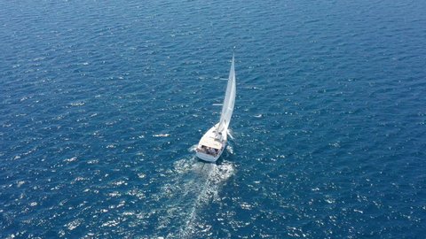 White sailboat on the sea. Leisure sailing on blue lake or ocean during summer vacation in the Mediterranean. Drone circling around a wind propelled yacht - aerial view: adventure, sport, luxury.