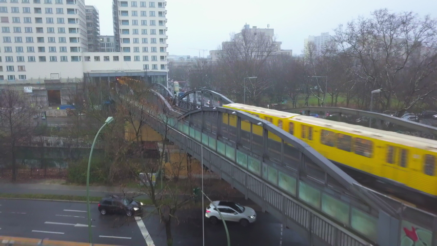 Aerial follow Shot of Yellow Subway Train on Bridge in Berlin entering Train Station, Foggy weather wirh clouds, Drone Shot