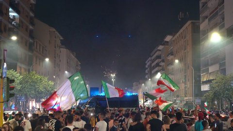 ROME, ITALY - JULY 11, 2021: Unforgettable celebration of victory in UEFA EURO 2020, streets of Rome full of happy fans with lifting hands and waving flags on background of fireworks in air