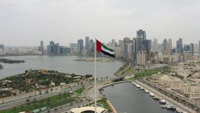 Aerial view of the Flag of the United Arab Emirates modern skyscrapers in the backgraound,  The national symbol of UAE over Sharjah's Flag Island, 4K Video