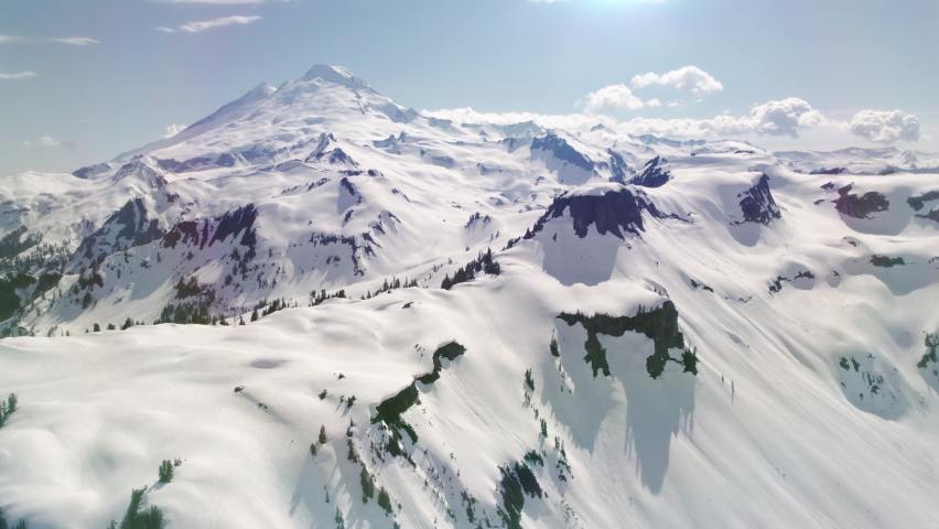 Snowy Mountain Environment Aerial Background with Hazy Lens Flare. Helicopter perspective slow floating away from picturesque Mount Baker during Spring season