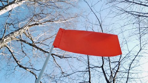 Slow motion red flag waving in the wind. Red flag on a background of sky and trees