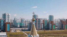 Religion and faith concept, aerial view of a golden cross on the top of the church. Video. Big golden cross on colorful houses and cloudy blue sky background.