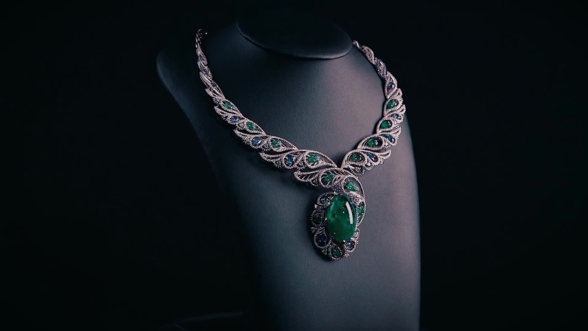 Beautiful necklace with blue sapphires and green emeralds on a black mannequin. Video. Close up of an expensive pendant of white gold and gemstones. Royalty-Free Stock Footage #1076017820