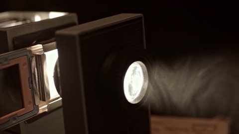 Close up of turning on retro slide projector in a dark room. Stock footage. Old fashioned vintage filmscope turned on n black background.