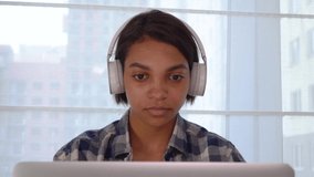 A happy female freelancer works on a laptop at home, listens to music with large headphones, and dances.