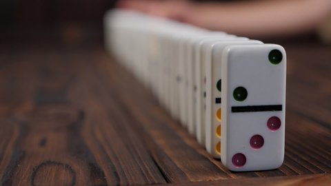 Close-up of a domino falling on a table, blurred background. The domino effect.