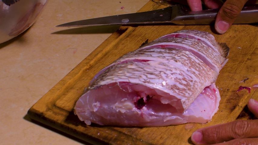 Chef Hands Cutting cubera snapper (Lutjanus cyanopterus) on wheels on wooden board
