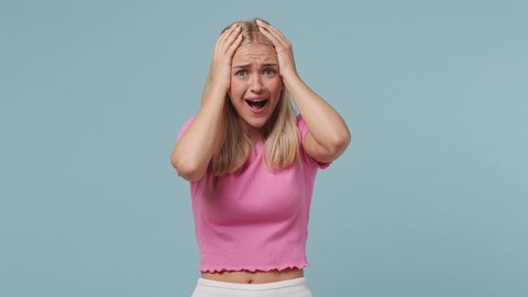 Joyful jubilant surprised shocked young blonde woman 20s wears pink t-shirt say wow omg what spread hands put arms on face screech isolated on pastel plain light blue color background studio portrait