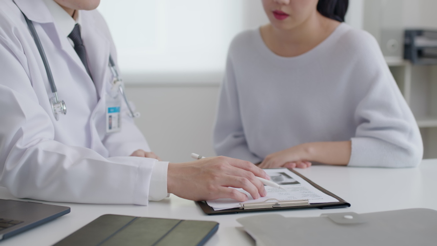 Friendly medic service people or asia male help talk discuss of medical exam record test result at clinic office desk. Young sad serious stress woman visit, follow , listen, see doctor at hospital. | Shutterstock HD Video #1076031770