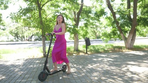 young millennial woman riding electric scooter in summer in a park, urban eco friendly means of transport, modern electric transport, contemporary electric vehicle . High quality 4k footage