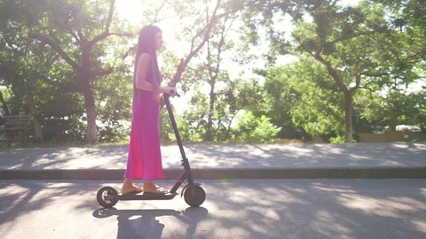young millennial woman riding electric scooter in summer in a park, urban eco friendly means of transport, modern electric transport, contemporary electric vehicle . High quality 4k footage