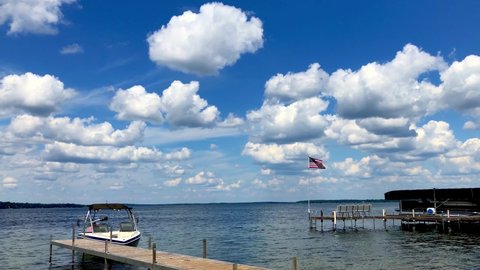 Beautiful Minnesota lake scene, as a boat pulls slowly up to the dock. A hand held clip with with an American flag waving over the nearby dock, and fluffy white clouds under a blue sky.
